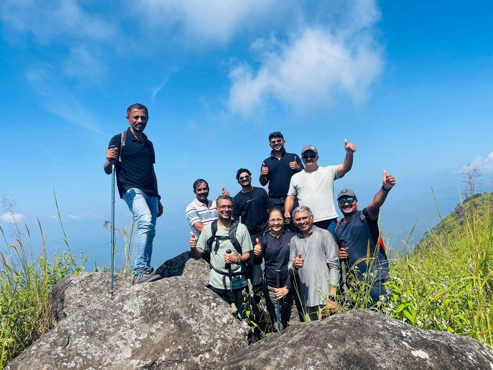 Trekking group celebrating at the Muthukora Mala summit with valley views behind, Kottayam