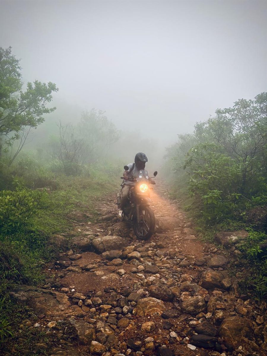 A rider on a misty, rocky off-road trail with the headlight glowing, near Yendayar, Kerala